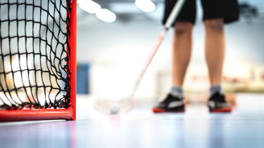 Bottom corner of hockey net with hockey players feet and stick